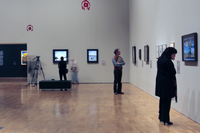 Installation view with 'The Age' art critic Associate Professor Robert Nelson at centre right and 'The hand. The remorse of conscience' 1930 at far right, from the 'Salvador Dalí: Liquid Desire' Winter Masterpieces exhibition at the National Gallery of Victoria, Melbourne