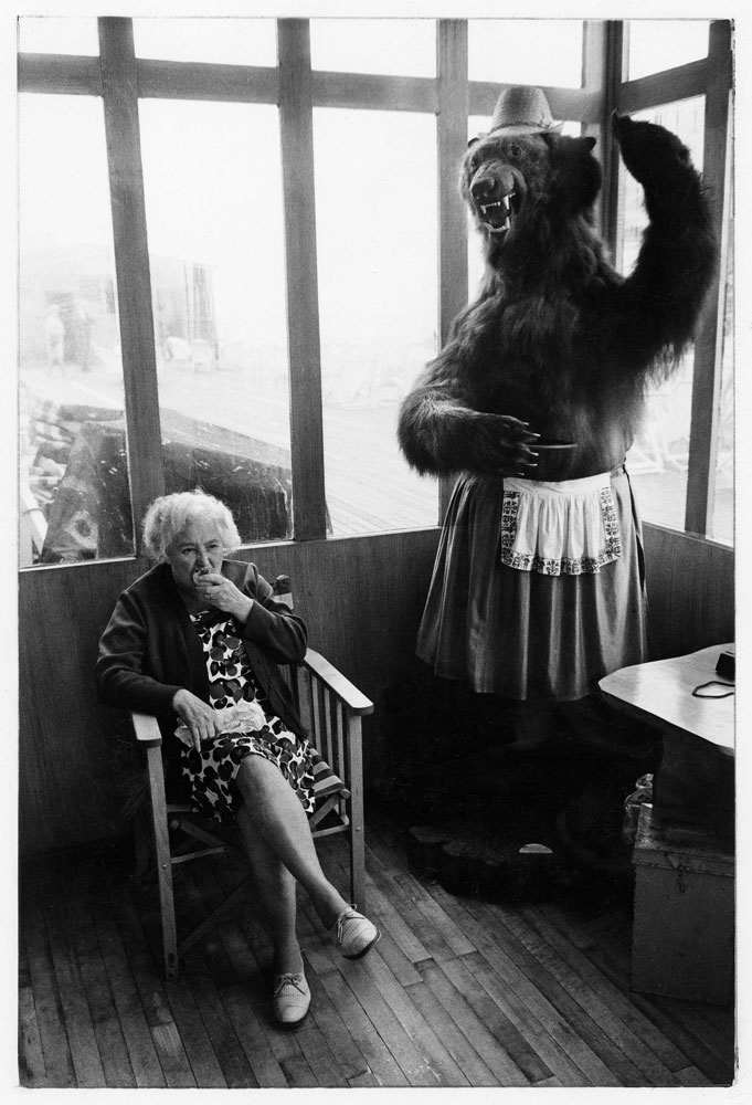 Tony Ray-Jones (English, 1941-1972) 'Elderly woman eating pie seated in a pier shelter next to a stuffed bear, 1969' 1969