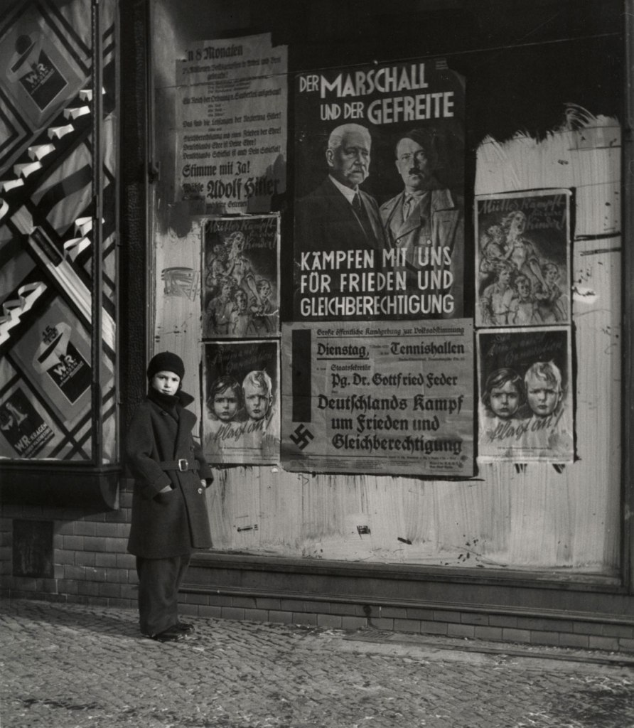 Roman Vishniac (Russian-American, 1897-1990) '[Vishniac's daughter Mara posing in front of an election poster for Hindenburg and Hitler that reads "The Marshal and the Corporal: Fight with Us for Peace and Equal Rights," Wilmersdorf, Berlin]' 1933