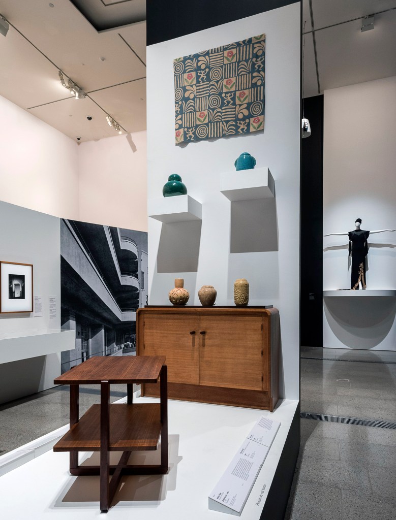 Installation view of the exhibition 'Brave New World: Australia 1930s' at NGVA with Max Dupain's 'Illustration for Kelvinator' advertisement at left and Ethel Blundell's 'Vase' centre on sideboard