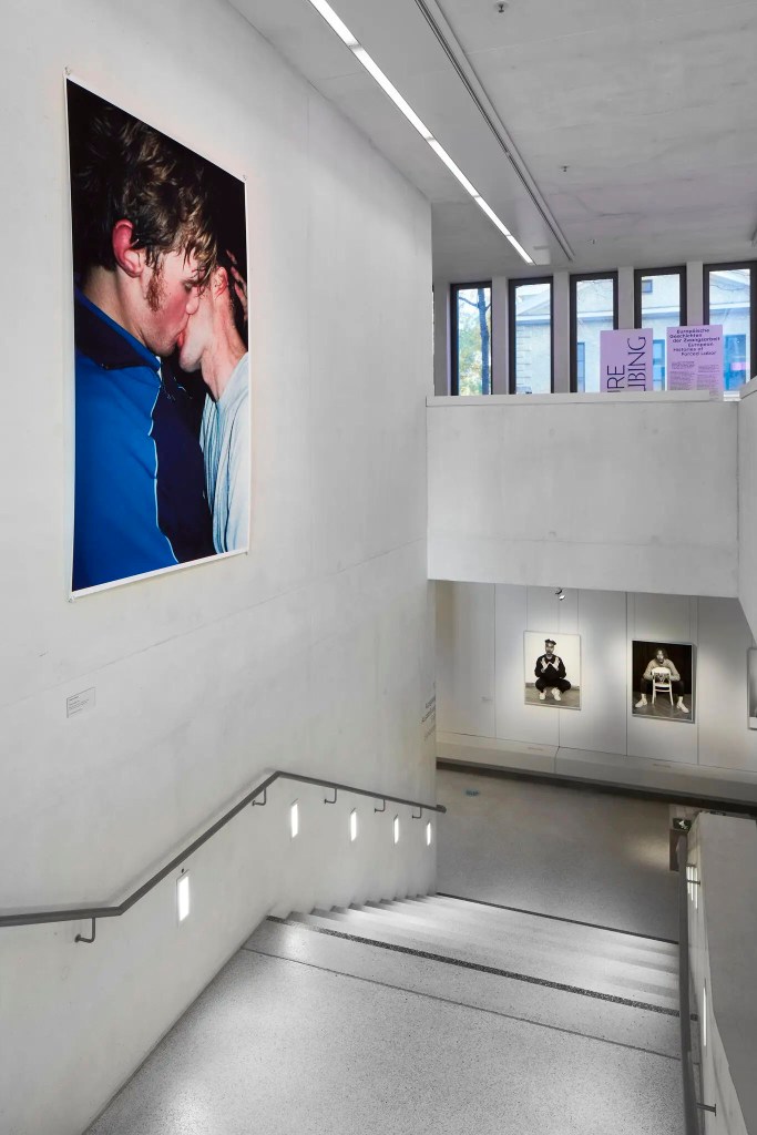 Installation view of the exhibition 'TO BE SEEN: Queer Lives 1900-1950' at the Munich Documentation Center for the History of National Socialism showing Wolfgang Tillmans's photograph 'The Cock (Kiss)' (2002) Installation view of the exhibition 'TO BE SEEN: Queer Lives 1900-1950' at the Munich Documentation Center for the History of National Socialism showing Wolfgang Tillmans's photograph 'The Cock (Kiss)' (2002)