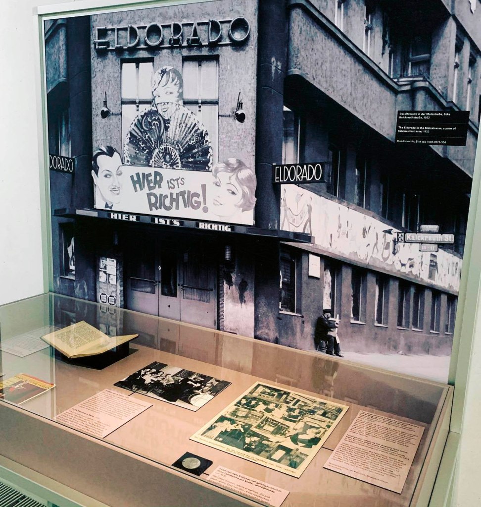 Installation view of the exhibition 'TO BE SEEN: Queer Lives 1900-1950' at the Munich Documentation Center for the History of National Socialism showing at rear, an enlargement of an image by an unknown photographer of the Eldorado in the Motzstrasse (1932); and at left centre in the display cabinet, an image by an unknown photographer Trans* people in the Eldorado in Berlin (1926) Installation view of the exhibition 'TO BE SEEN: Queer Lives 1900-1950' at the Munich Documentation Center for the History of National Socialism showing at rear, an enlargement of an image by an unknown photographer of the Eldorado in the Motzstrasse (1932); and at left centre in the display cabinet, an image by an unknown photographer Trans* people in the Eldorado in Berlin (1926)