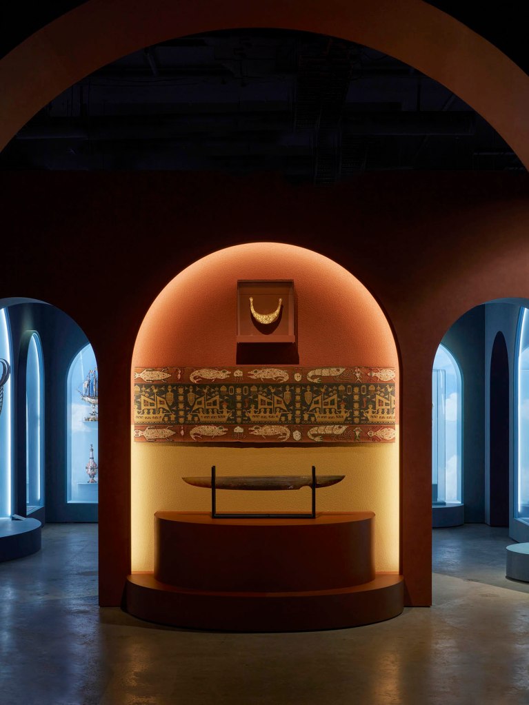 Installation view of the exhibition '1,001 Remarkable Objects' at Powerhouse Ultimo, Sydney showing at top, Man's ceremonial headpiece (lamba), sheet gold alloy, Sumba, Indonesia, 1880-1950; and at second top, Textile length (mens waist cloth), handwoven cotton / shells / beads, maker unknown, East Sumba, Indonesia, 2000-2004