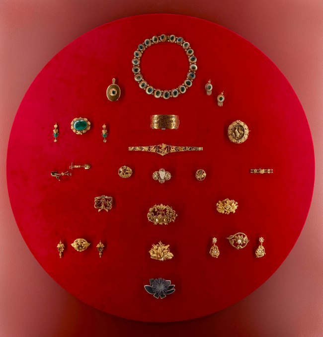 Installation view detail of the exhibition '1,001 Remarkable Objects' at Powerhouse Ultimo, Sydney showing examples of 19th century Australian gold jewellery in the Powerhouse Collection including at top, a parure comprising necklace, locket and earrings (pair), gold / operculum by F Allerding & Son, Sydney, New South Wales, Australia, 1879-1884; and at second top centre, Bangle, 'Soyons toujours unis / Par un divin amour', 18 carat gold, Henry Steiner, Adelaide, South Australia, c. 1878