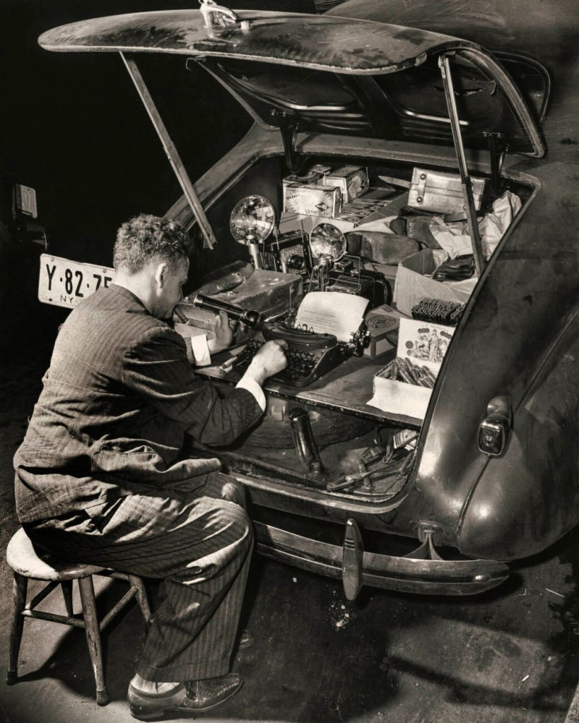 Weegee (American, 1899-1968) '"Chevrolet". Weegee in front of his typewriter, installed in the trunk of a 1938 Chevrolet, New York' c. 1943 from the exhibition 'Weegee, Autopsy of the Spectacle' at the Foundation Henri Cartier-Bresson, Paris, January - May, 2024
