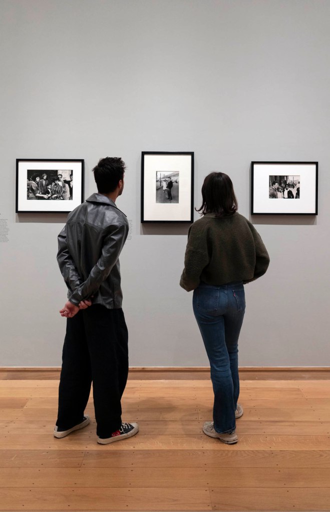Installation view of the exhibition 'Roger Mayne: Youth' at the Courtauld Gallery, London showing at left, Mayne's 'Teenagers, Soho Fair, London' (17 July 1958); at centre, 'Teenage Couple, Absolute Beginners photo-shoot' (26 April 1959); and at right, 'Men and boys, Southam Street, London' (1959)